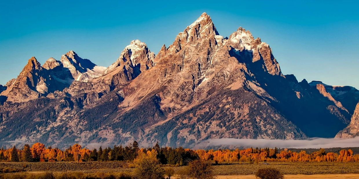 Majestic mountain range with autumn trees and clear blue sky.