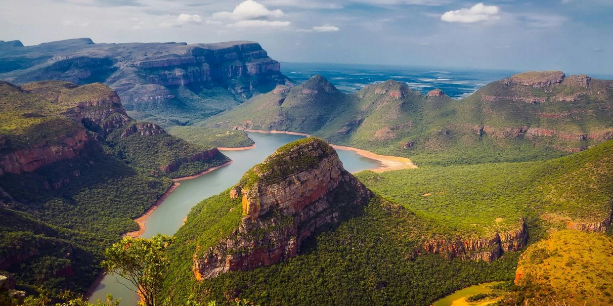 Scenic view of a winding river surrounded by lush green mountains under a blue sky.