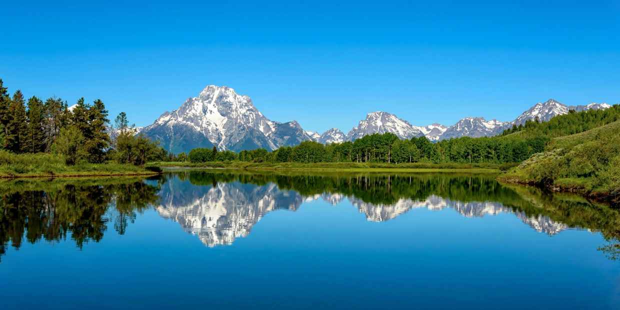 Snow-capped mountains reflecting in a calm lake under a clear blue sky.
