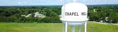White water tower labeled “CHAPEL HILL” overlooking green fields and trees.