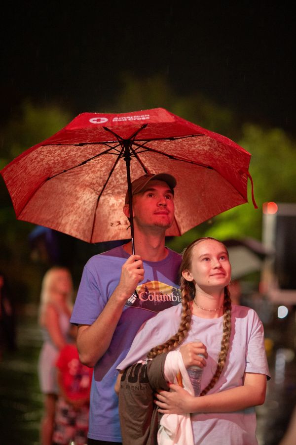 Man and girl under a red umbrella at night.