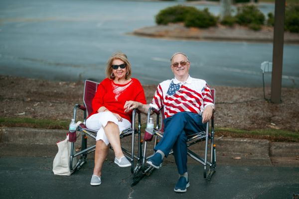 Elderly couple sitting outdoors holding hands and smiling.
