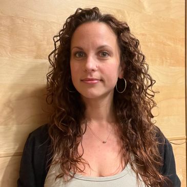 Woman with curly hair posing against a wooden background.