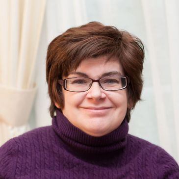 Smiling woman with glasses in a purple sweater.