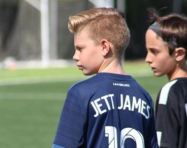 Two young boys standing on a soccer field, one wearing a jersey with 'Jett James' and number 10.