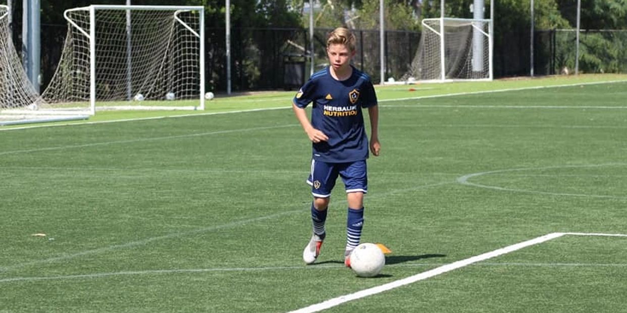 Young soccer player in blue jersey dribbling a ball on a green field.