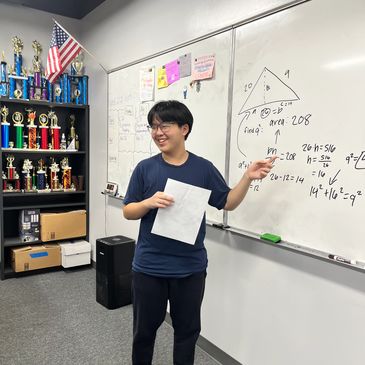 Student giving math presentation in classroom with trophies and American flag.