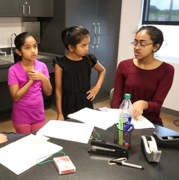 A group of children and a teacher discussing papers at a table.