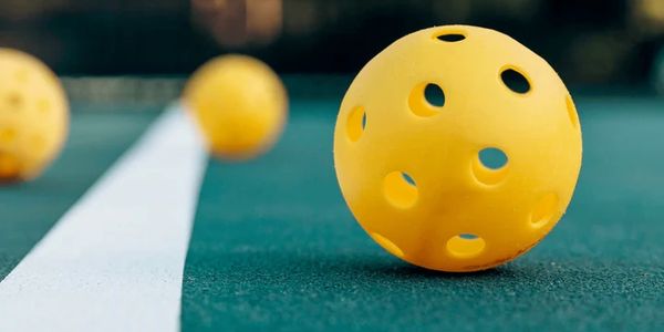 Close-up of yellow perforated balls on a green surface with a white line.