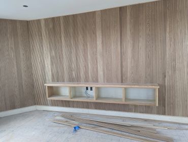 Wooden slat wall with floating shelf under construction.