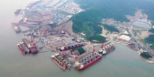 A large shipyard with multiple vessels docked and cranes in operation.
