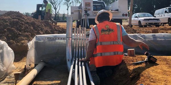 Worker in orange vest managing conduit pipes at construction site.