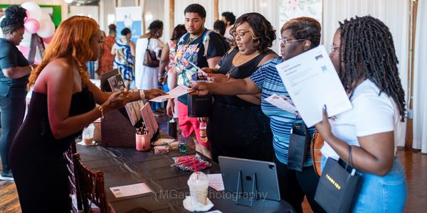 People exchanging information at an indoor event booth with informational materials.