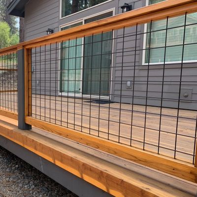Modern wooden deck with metal grid railing attached to a gray house.