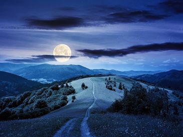 A full moon over a mountainous landscape at night.