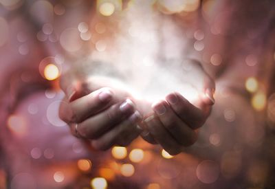 Hands cupping a glowing light with bokeh effects.