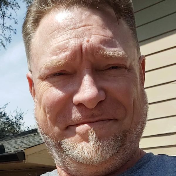 Close-up of a man with a beard smiling outdoors on a sunny day.