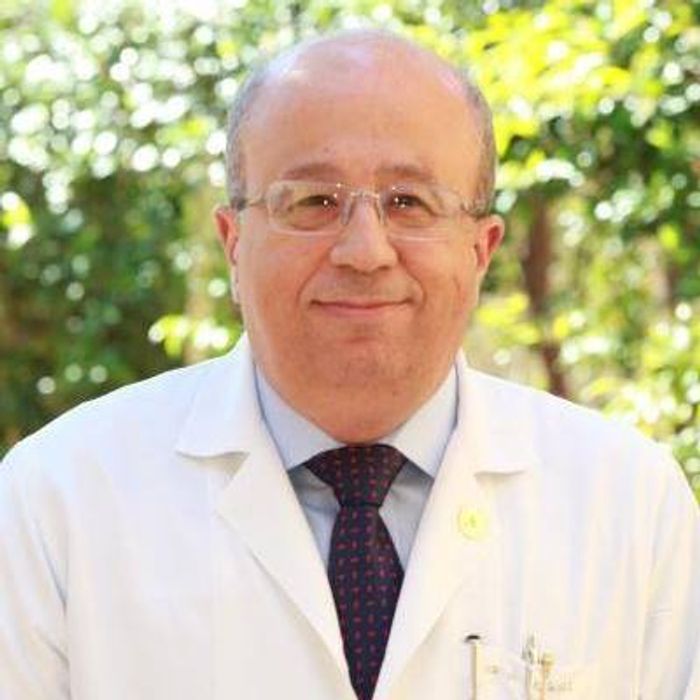 Smiling male doctor in white coat and glasses outdoors.