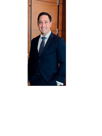 Man in a navy blue suit smiling, standing indoors.