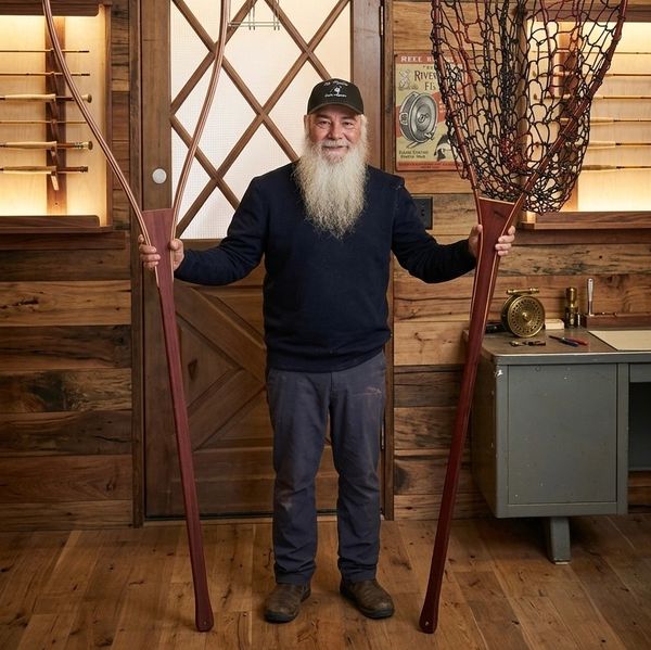 A man holding an oversized fishing net and rod indoors.