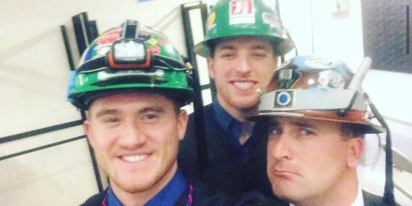 Three men wearing decorated hard hats smiling indoors.