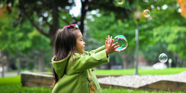 A young girl reaches out to catch soap bubbles in a park.