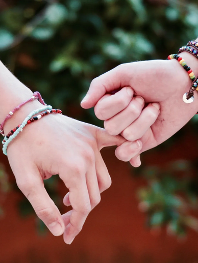 Two people linking pinkies, wearing colorful beaded bracelets.