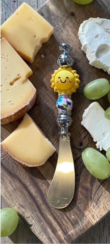 Cheese board with a smiling sun-themed spreader and grapes.