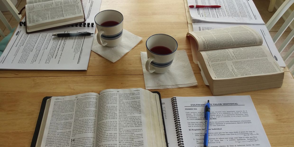 Books, papers, two cups of tea, and pens on a wooden table.