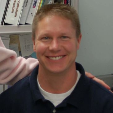 Smiling man in a navy polo shirt indoors.