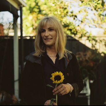 Smiling woman holding a sunflower outdoors in soft sunlight.