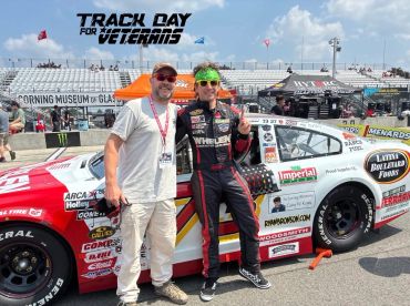 Two men posing next to a race car on a sunny day at a racing event.