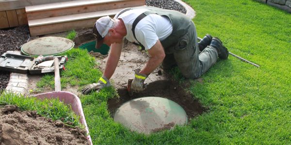 Man installing or maintaining a septic tank cover in a yard.