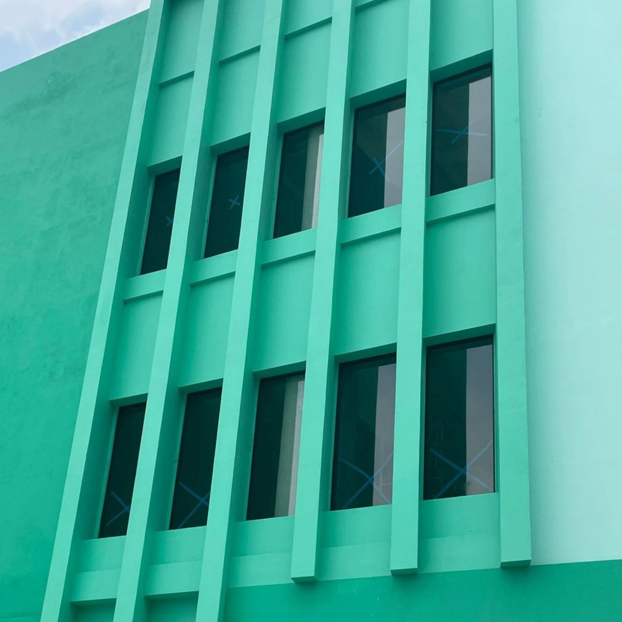 Green building facade with vertical beams and windows.