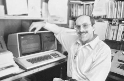 Man smiling with an old computer in a vintage office.