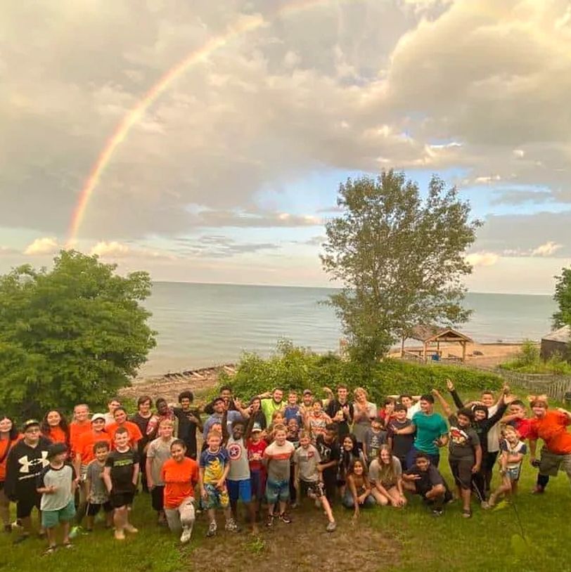 Group of people posing outdoors with a rainbow over water.