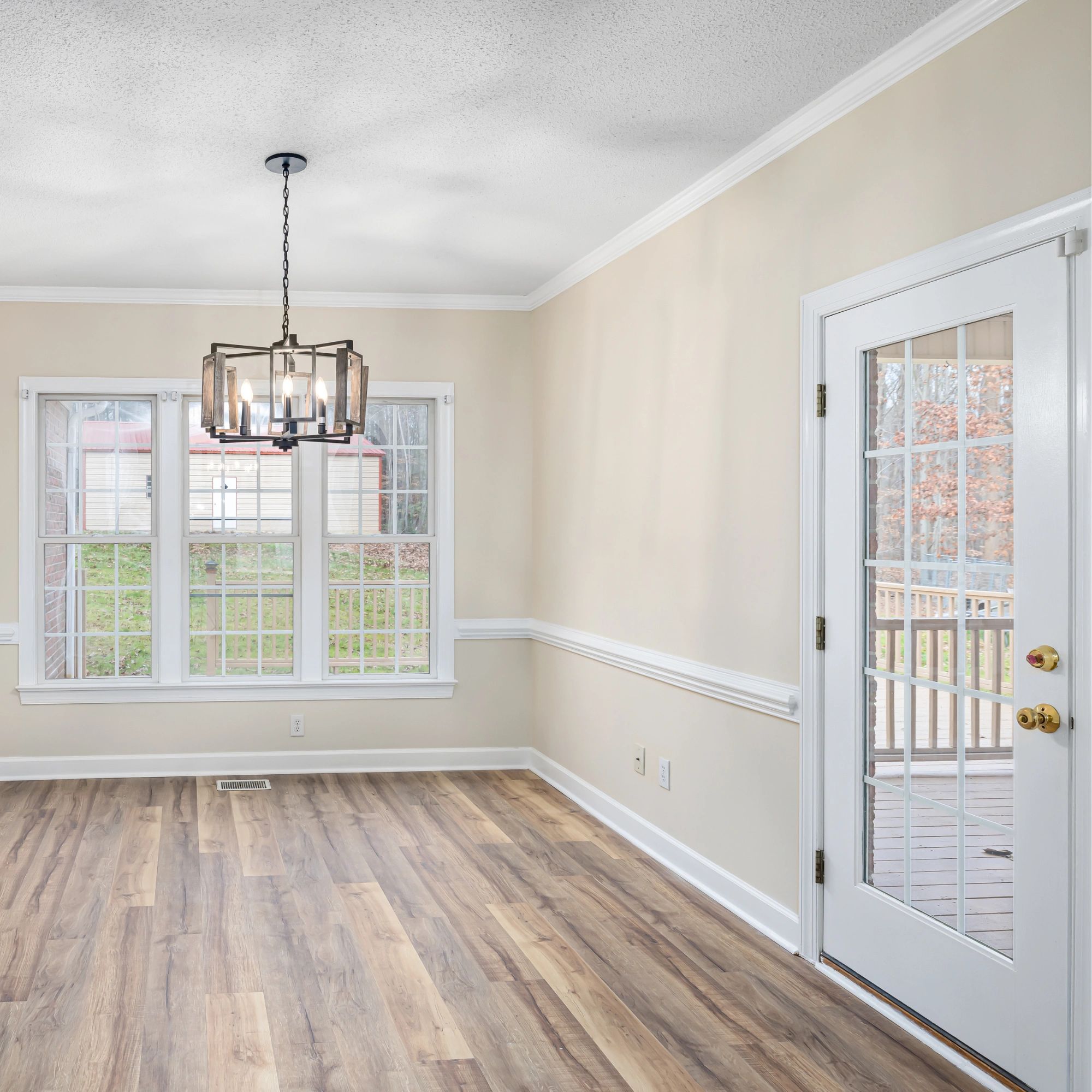 Empty room with wooden floor, chandelier, and glass door leading outside.