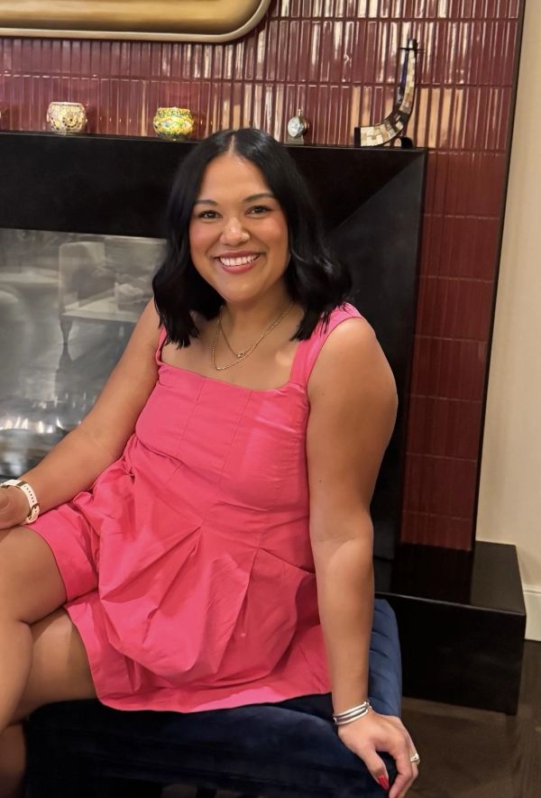 Smiling woman in pink dress sitting indoors.