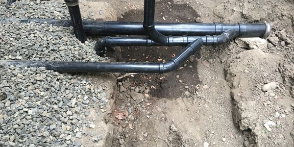 Black plastic plumbing pipes laid in dirt and gravel trench.