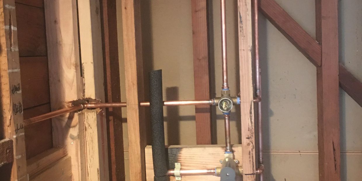 Copper plumbing pipes installed on wooden framing in a wall.