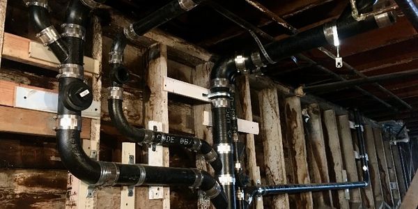 Black plumbing pipes installed against wooden beams in a building under construction.