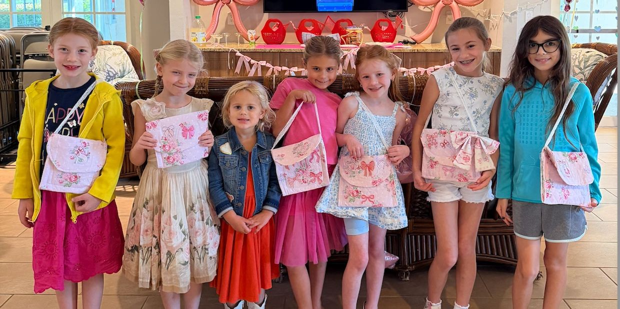 Seven young girls posing with handmade floral bags and dresses at a party.