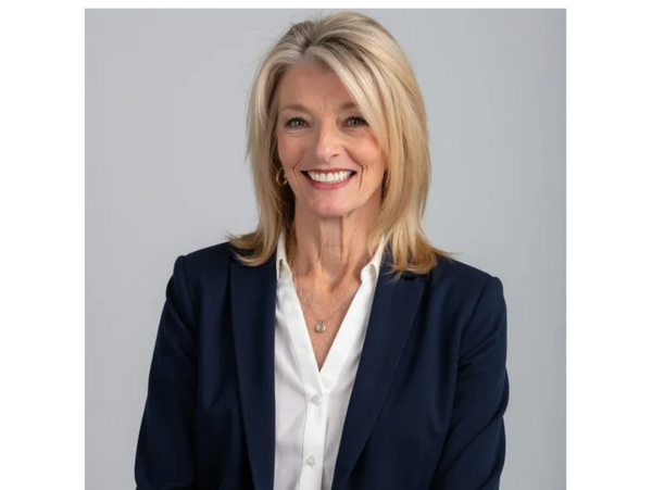 Confident woman in business attire smiling against a neutral background.