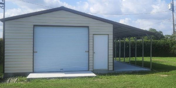 Metal garage with a roll-up door and adjacent covered carport on a sunny day.