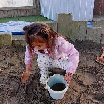 A young girl playing in a sandbox with a bucket and shovel.