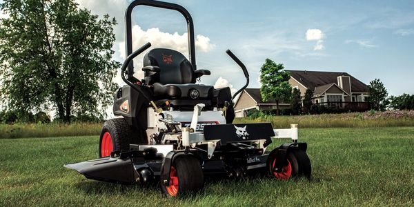 A black and red riding lawn mower on a grassy field near houses.