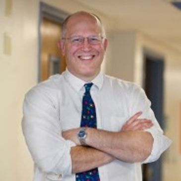 Smiling man in white shirt and colorful tie with arms crossed.
