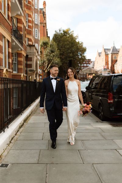 Newlywed couple joyfully walking hand in hand on a city sidewalk.