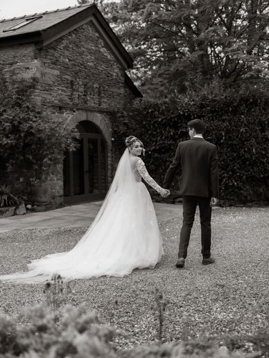 Bride and groom holding hands walking outside a rustic stone building.