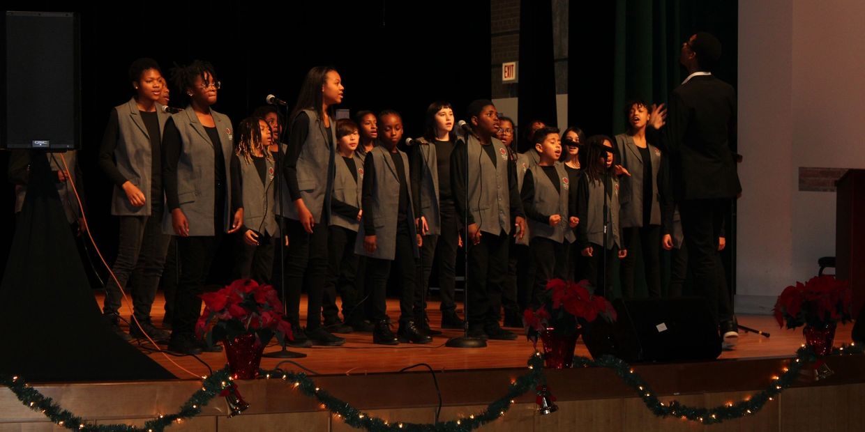 A children's choir performing on stage with a conductor leading.